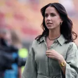 Maja Strzelczyk w oliwkowej koszuli, z naszyjnikami i złotym zegarkiem, na tle stadionu.