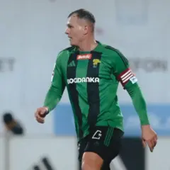 Piłkarz Górnika Łęczna w zielonej koszulce z czarnymi pasami, gotowy do gry przeciwko GKS Tychy.