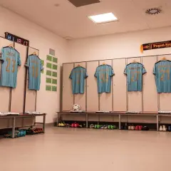 Szczecińska Pogoń gotowa do meczu z Cracovią. Koszulki zawodników wiszą w szatni, obok piłka i buty.