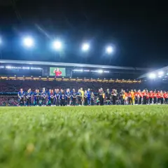 Piłkarze Wisły Kraków i Miedzi Legnica stoją na murawie przed meczem. Stadion wypełniony kibicami, nocne oświetlenie.