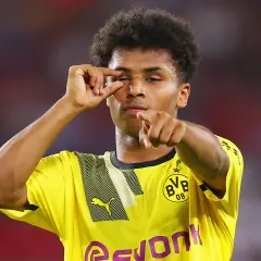 Piłkarz Borussii Dortmund w żółtej koszulce z czarnymi wzorami, wykonujący gest palcami przy oku i wskazujący palcem.