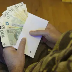 Dłonie trzymające kopertę z polskimi banknotami.