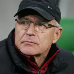 Lenczyk, trener piłkarski, w okularach i czapce, z uwagą obserwuje grę.