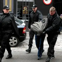 Ochroniarze w czarnych kurtkach i czapkach wyprowadzają mężczyznę owiniętego w koc. Może to być interwencja wobec kiboli.