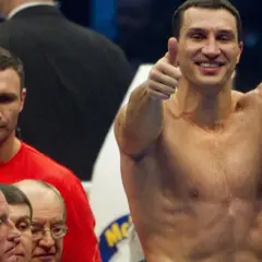 Uśmiechnięty Witalij Kliczko pokazuje kciuk w górę, podczas gdy jego brat Władymir stoi obok.