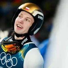Uśmiechnięty zawodnik w kasku z polską flagą, gotowy po zdobyciu medali. Tomasiak w akcji, celuje w kolejne zwycięstwa.