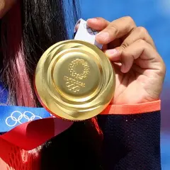 Złote medale olimpijskie z Tokio 2020, symbol ciężkiej pracy i zwycięstwa, błyszczą w dłoniach sportsmenki.
