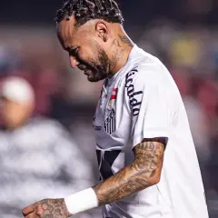 Neymar w białej koszulce Santos, z tatuażami na ramieniu, wygląda na zamyślonego. To właśnie tam gra Neymar.