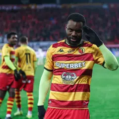 Piłkarz w żółto-czerwonej koszulce pozdrawia kibiców. W tle inni zawodnicy i trybuny. Mecz Widzew Łódź – Jagiellonia Białystok.