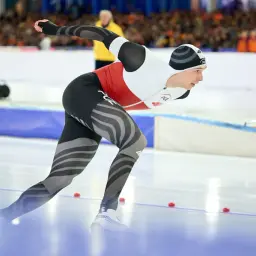 Paweł Kania w akcji na lodowisku, w aerodynamicznym stroju z biało-czerwonym panelem.