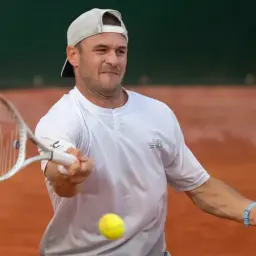 Gracz w **paul tenis** uderza piłkę rakietą na korcie ziemnym.