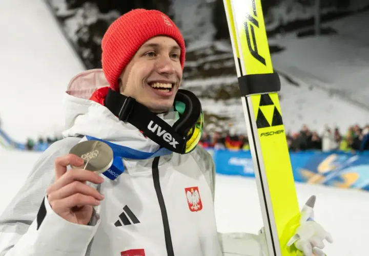 Uśmiechnięty skoczek narciarski w czerwonej czapce trzyma srebrny medal. Polacy na Igrzyskach 2026 z pewnością będą walczyć o kolejne laury!