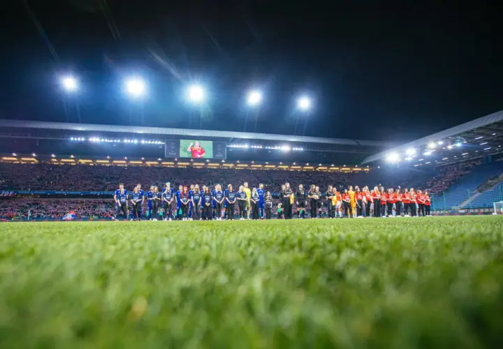 Piłkarze Wisły Kraków i Miedzi Legnica stoją na murawie przed meczem. Stadion wypełniony kibicami, nocne oświetlenie.
