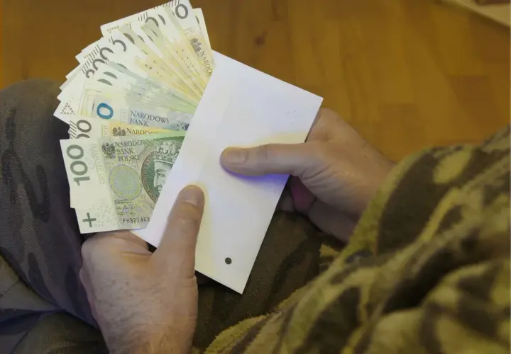 Dłonie trzymające kopertę z polskimi banknotami.
