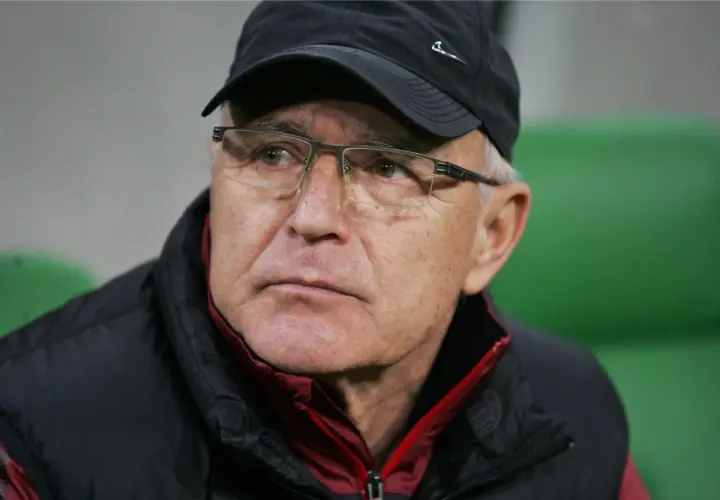 Lenczyk, trener piłkarski, w okularach i czapce, z uwagą obserwuje grę.
