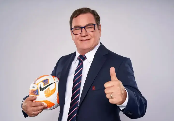 Uśmiechnięty trener reprezentacji Polski w garniturze trzyma piłkę i pokazuje kciuk w górę.