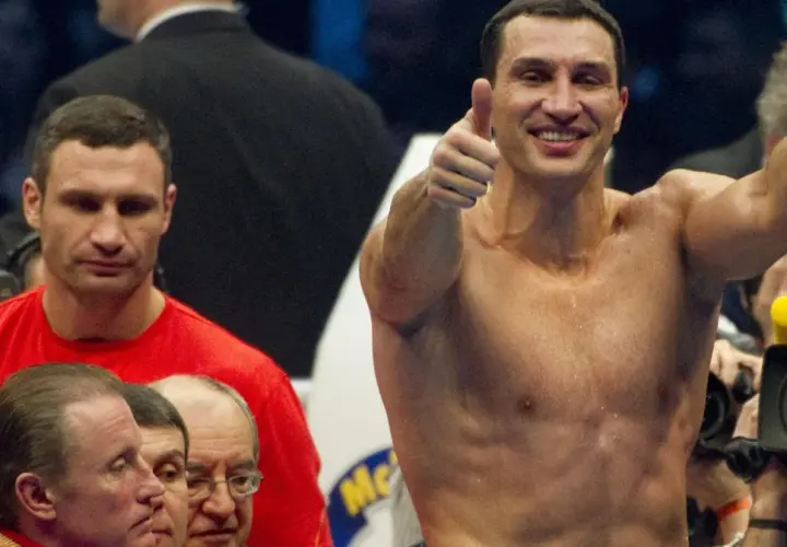 Uśmiechnięty Witalij Kliczko pokazuje kciuk w górę, podczas gdy jego brat Władymir stoi obok.
