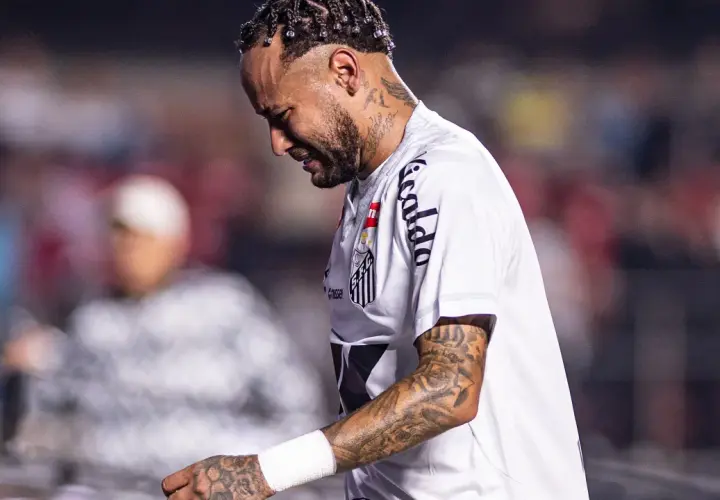 Neymar w białej koszulce Santos, z tatuażami na ramieniu, wygląda na zamyślonego. To właśnie tam gra Neymar.