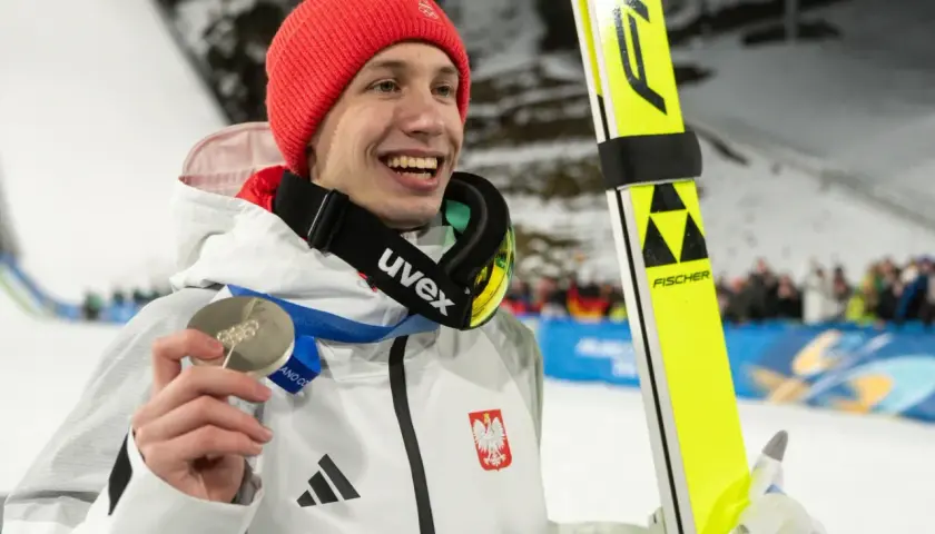 Uśmiechnięty skoczek narciarski w czerwonej czapce trzyma srebrny medal. Polacy na Igrzyskach 2026 z pewnością będą walczyć o kolejne laury!