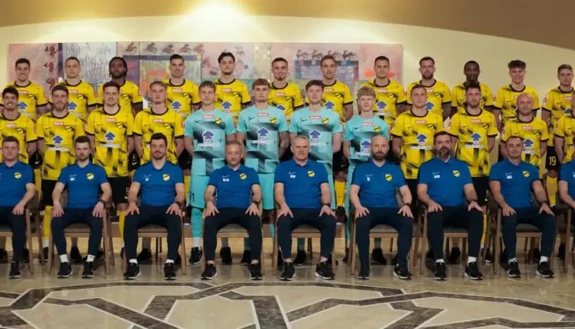 Drużyna piłkarska Wieczysta Kraków w komplecie. Zawodnicy i sztab szkoleniowy pozują do wspólnego zdjęcia w strojach klubowych.