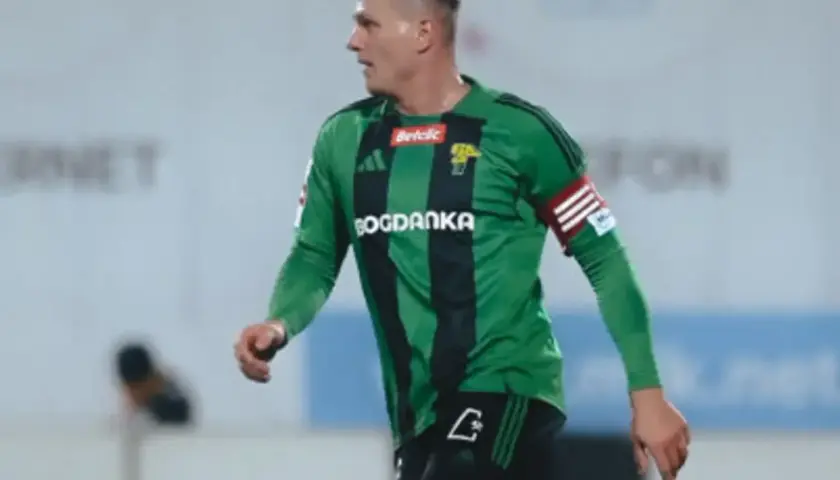 Piłkarz Górnika Łęczna w zielonej koszulce z czarnymi pasami, gotowy do gry przeciwko GKS Tychy.