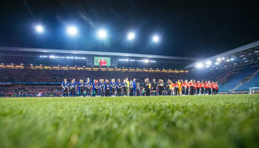 Piłkarze Wisły Kraków i Miedzi Legnica stoją na murawie przed meczem. Stadion wypełniony kibicami, nocne oświetlenie.