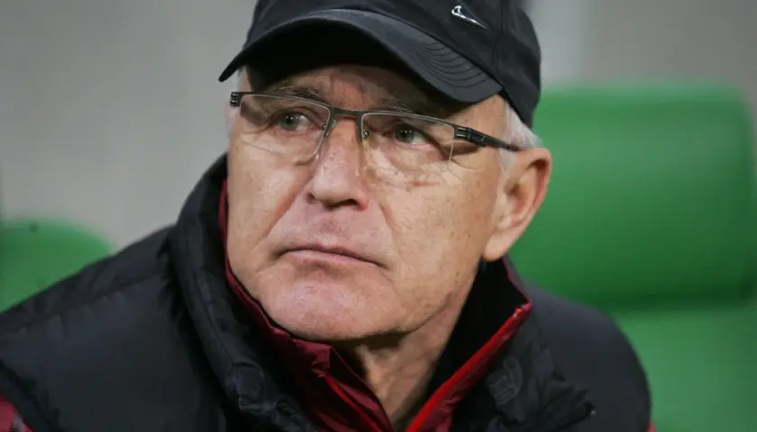 Lenczyk, trener piłkarski, w okularach i czapce, z uwagą obserwuje grę.