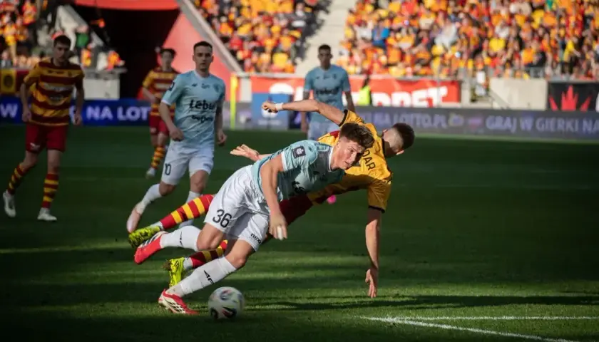 Zacięta walka o piłkę podczas meczu Jagiellonia Białystok – Piast Gliwice. Dwóch zawodników walczy o panowanie nad futbolówką na murawie.