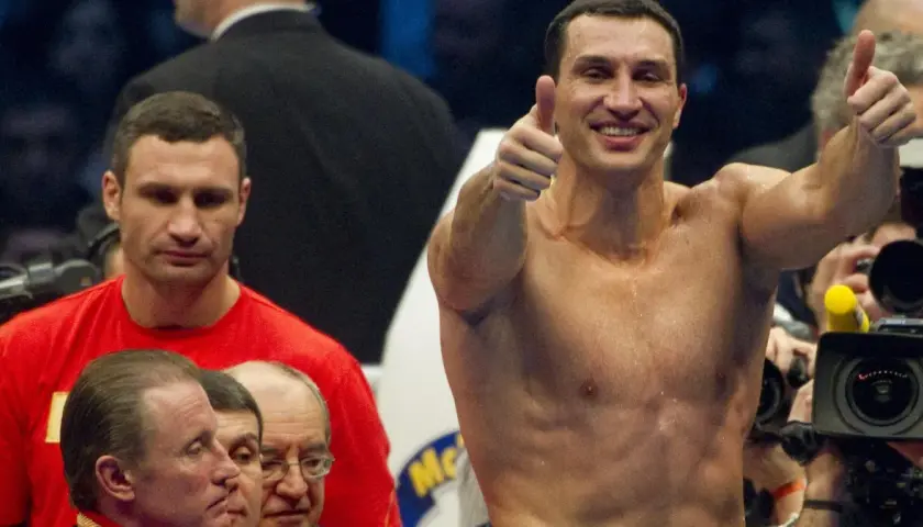 Uśmiechnięty Witalij Kliczko pokazuje kciuk w górę, podczas gdy jego brat Władymir stoi obok.