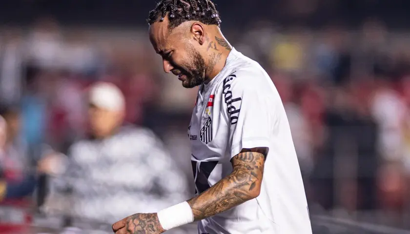 Neymar w białej koszulce Santos, z tatuażami na ramieniu, wygląda na zamyślonego. To właśnie tam gra Neymar.