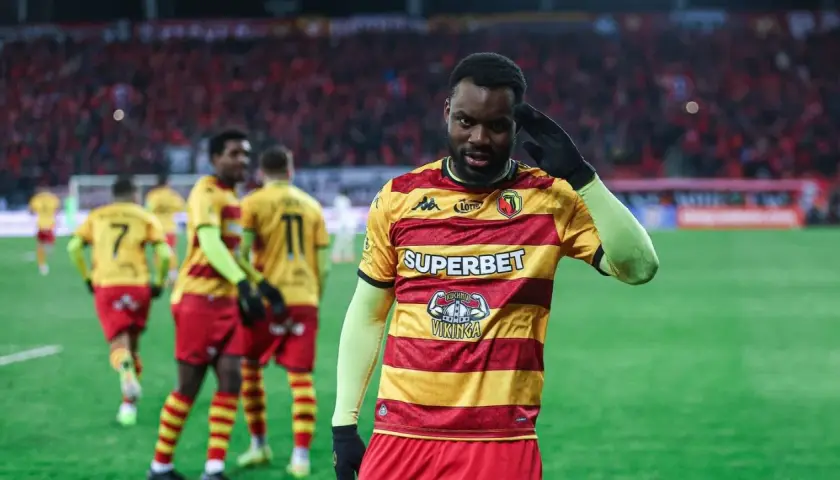 Piłkarz w żółto-czerwonej koszulce pozdrawia kibiców. W tle inni zawodnicy i trybuny. Mecz Widzew Łódź – Jagiellonia Białystok.