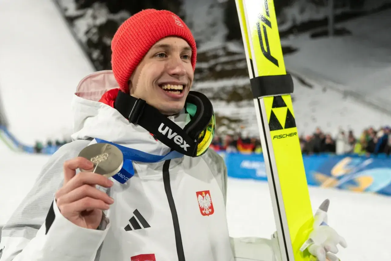 Uśmiechnięty skoczek narciarski w czerwonej czapce trzyma srebrny medal. Polacy na Igrzyskach 2026 z pewnością będą walczyć o kolejne laury!