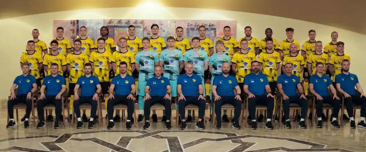 Drużyna piłkarska Wieczysta Kraków w komplecie. Zawodnicy i sztab szkoleniowy pozują do wspólnego zdjęcia w strojach klubowych.