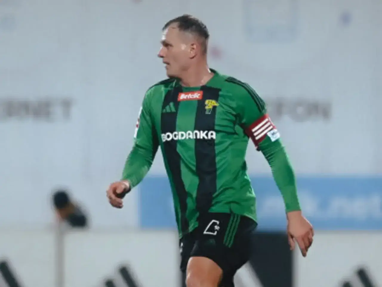 Piłkarz Górnika Łęczna w zielonej koszulce z czarnymi pasami, gotowy do gry przeciwko GKS Tychy.