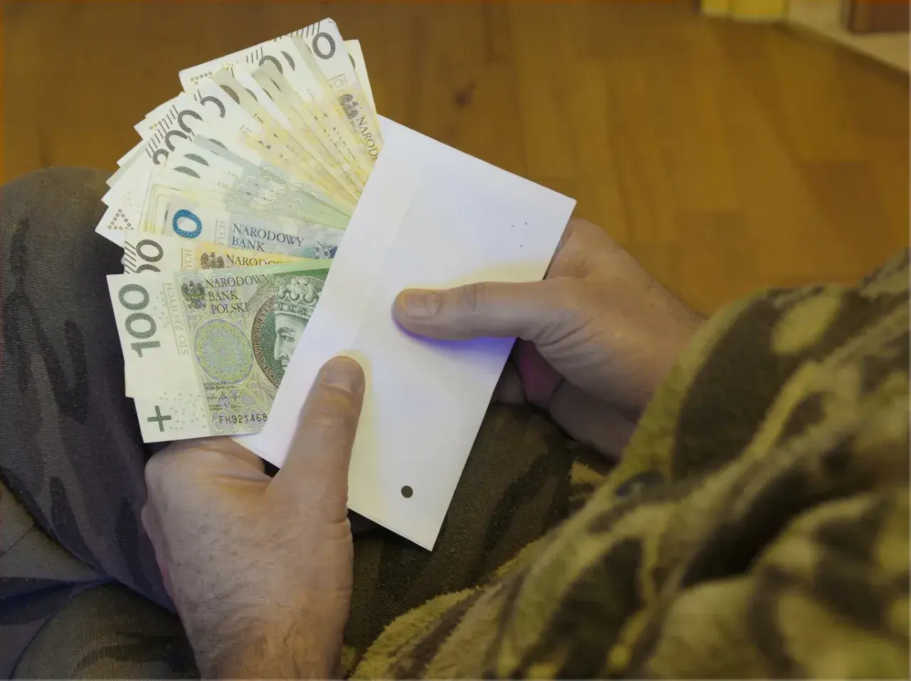 Dłonie trzymające kopertę z polskimi banknotami.