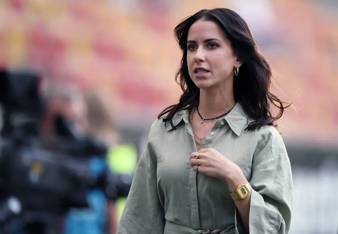 Maja Strzelczyk w oliwkowej koszuli, z naszyjnikami i złotym zegarkiem, na tle stadionu.