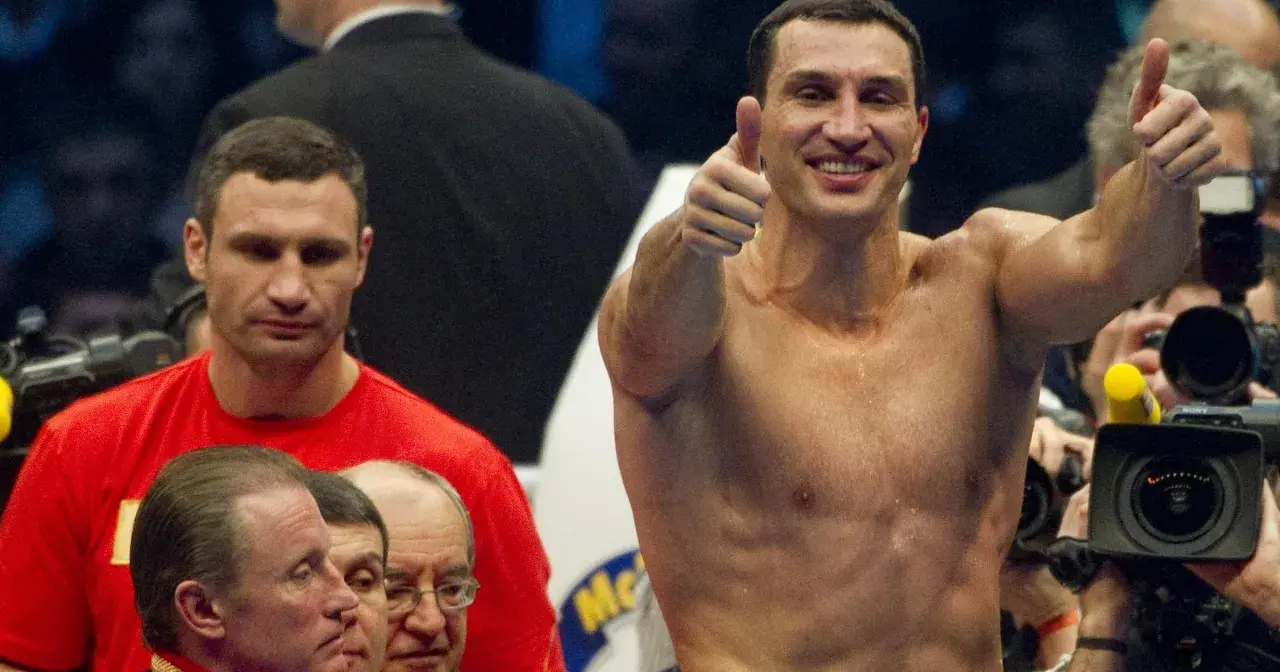 Uśmiechnięty Witalij Kliczko pokazuje kciuk w górę, podczas gdy jego brat Władymir stoi obok.