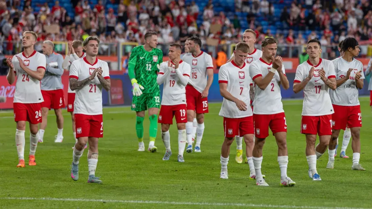 Piłkarze w białych strojach z orzełkiem na piersi, być może przyszli mistrzowie polski w piłce nożnej, stoją na murawie.