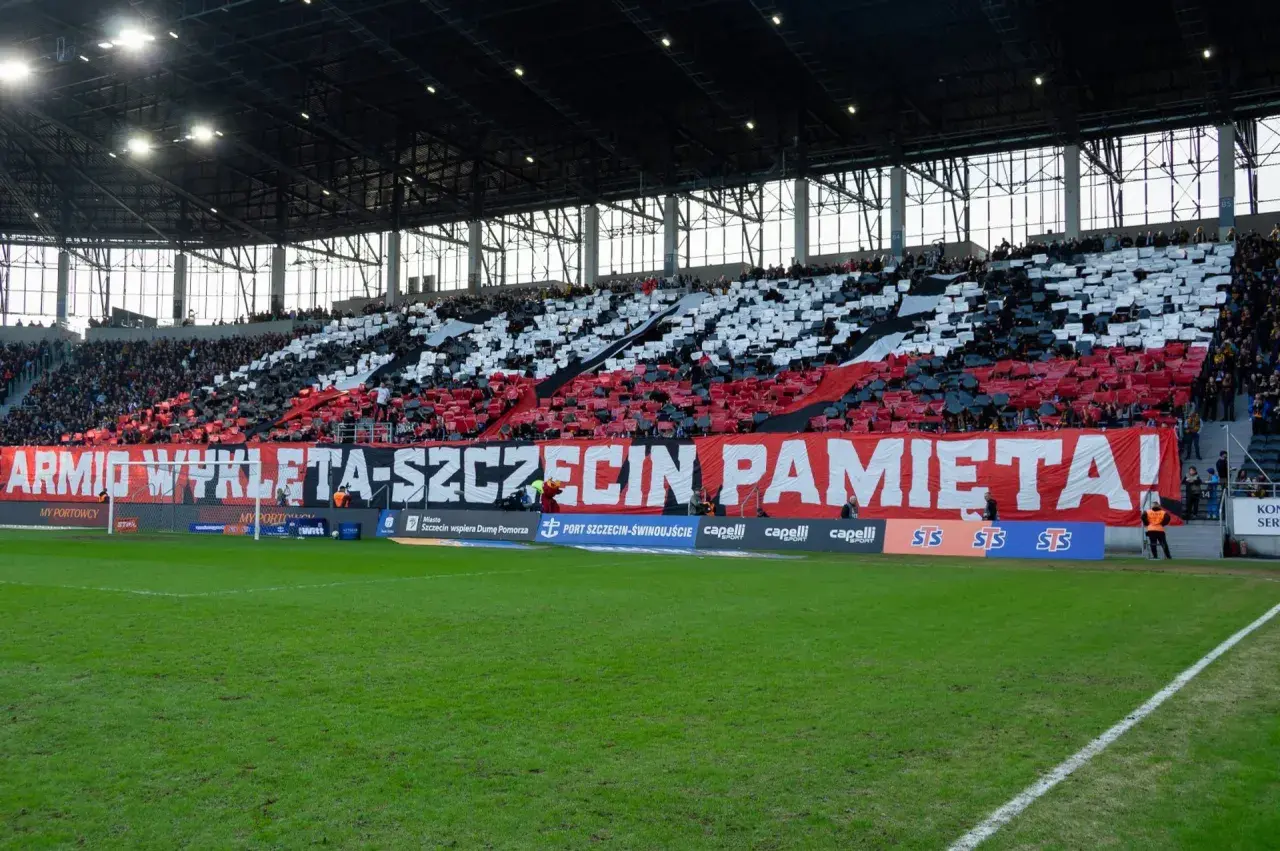 Trybuna stadionu podczas meczu Pogoń Szczecin – Widzew Łódź. Kibice tworzą biało-czerwony transparent "ARMIO WYKLETA-SZCZECIN PAMIĘTA!".