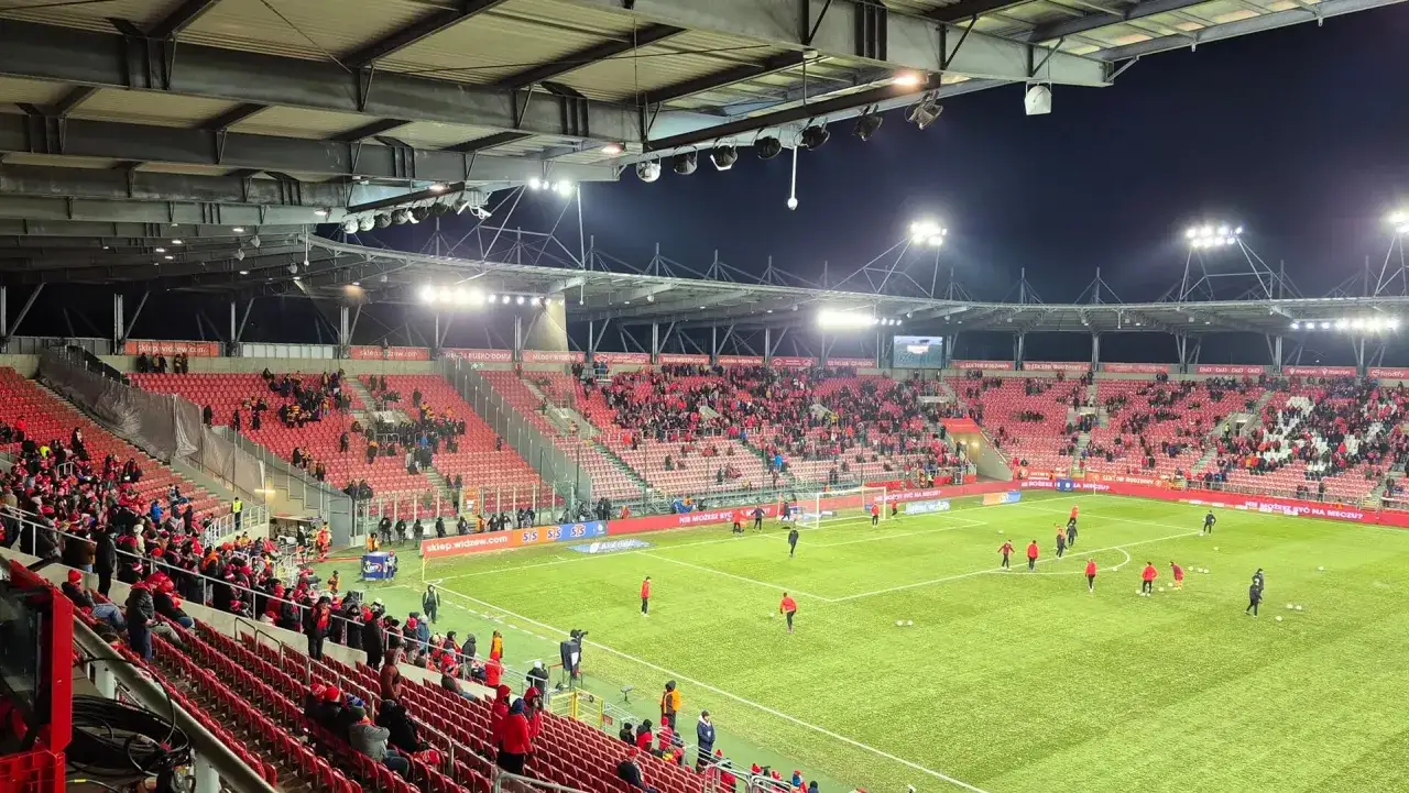 Stadion Widzewa Łódź przed meczem z Jagiellonią Białystok. Kibice na trybunach, piłkarze na murawie.