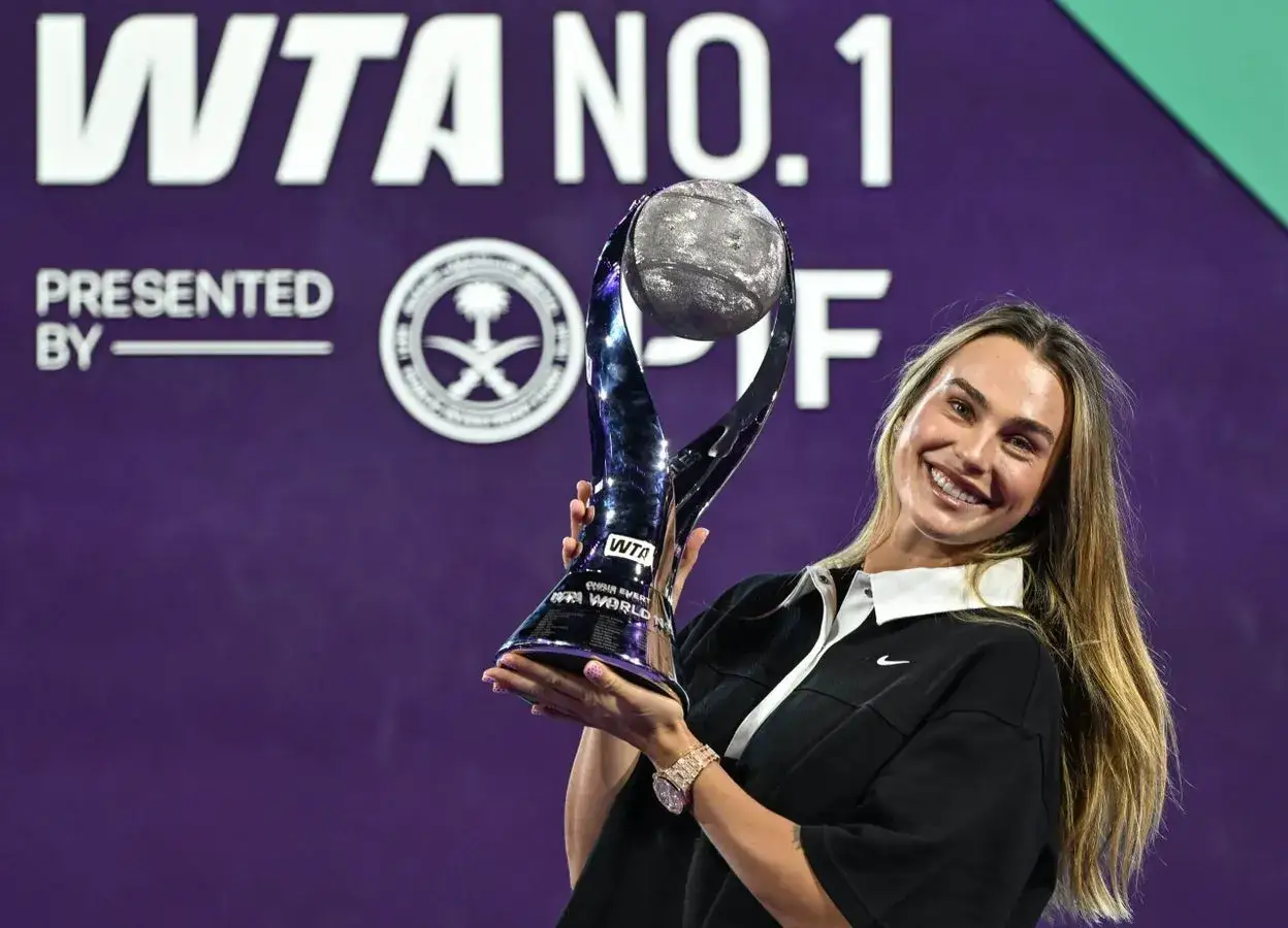 Uśmiechnięta tenisistka z pucharem WTA No. 1, symbolizującym jej pozycję w rankingu tenisistów.